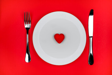 red heart on white plate, knife and fork on red background. Romantic table setting for Valentines...