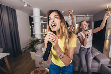 Group of young women spend free time in karaoke, sing and have fun together, with friends, at home.