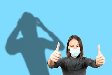 Latin woman wearing a face mask pretending to be ok with the thumbs up while her shadow shows her...