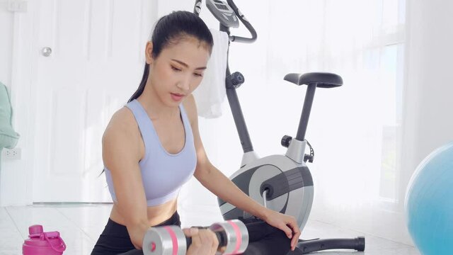 Young asian sporty woman lifting weight and working on her biceps at home.