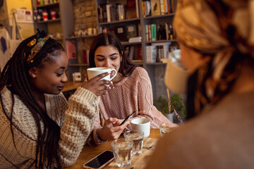 Three young multi ethnic women enjoy coffee at a coffee shop.