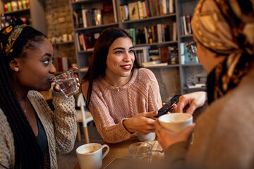 Three young multi ethnic women enjoy coffee at a coffee shop.