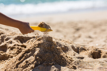 Child hand playing with sand with yellow shovel on a beach.