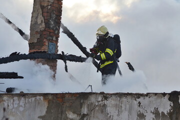 Firefighters with breathing apparatus masks extinguish the burning roof of a family house using...