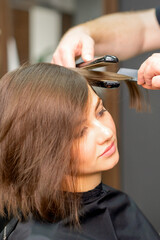 Fototapeta premium A male hairdresser is straightening the hair of the young woman in a beauty salon