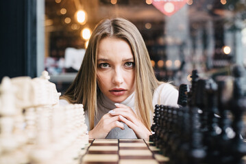 Beautiful girl play chess, queen’s gambit play and everyone wins, a smart and pensive face. White...