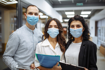 Fototapeta na wymiar Portrait of three office workers wearing medical masks discussing business and future prospects. New normal, health care, office hygiene concept. Coronavirus quarantine, pandemic, spread prevention.