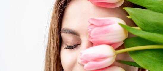 Half face portrait of a happy young caucasian woman with closed eyes and pink tulips cover her face against a white background