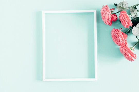 Beautiful flowers composition. White photo frame, pink rose flowers on pastel mint background. Valentines Day, Easter, Birthday, Happy Women's Day, Mother's day. Flat lay, top view, copy space