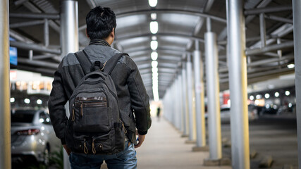 The back picture of a young man with a slanted bag walking to a shopping mall late at night.