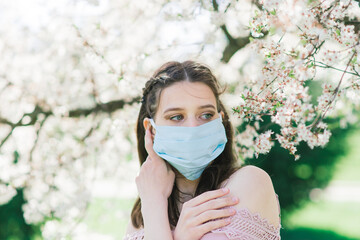 A girl in protective medical mask in spring among the blooming garden. Spring allergy conception