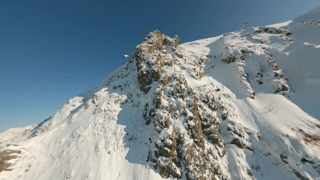 Herd mountain chamois running along slope on snowy mountain aerial view in sunny day. Gazex pipes for snow on winter mountain in ski resort view from fpv sport drone.