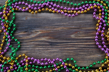 A frame of three colors of Mardi gras beads on wooden background