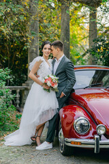 Gorgeous wedding couple. Wedding for two. The bride and groom hug next to a red car against the backdrop of a tropical garden.