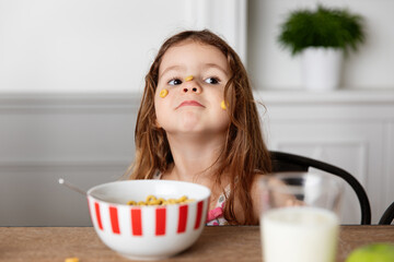 Goofy little girl with cereal stuck on face at kitchen table