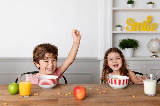Happy siblings eating cereals at kitchen table