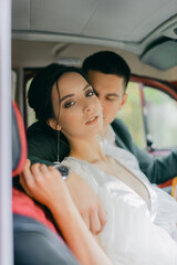 Gorgeous wedding couple. Wedding for two. Husband and wife are sitting and hugs inside a red retro car.