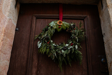 Classic Christmas wreath, decoration, Front view of a traditional Christmas crown made of evergreen branches, Holly leaves and berries hanging on rope nailed on an old wooden front door