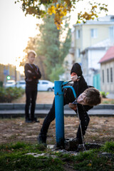 Boys on a walk drink water from a water pump on a city street