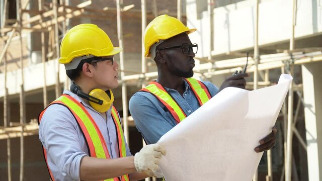 asian foreman and african american architect discuss with blueprint outdoors on construction site at village . contractor worker Inspection with builder . Engineer and foreman . quality control