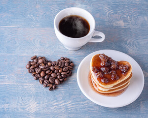 Breakfast for a lover. Homemade heart shaped pancakes with berry jam, heart shape made from coffee beans, white cup of hot coffee on a blue wooden table