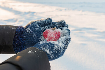 Hands in knitted warm gloves hold a red heart, against the background of winter, Valentine's day concept.