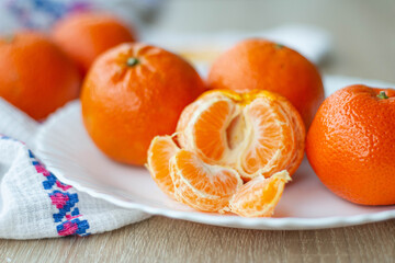 Slices of peeled mandarin lie on a plate, against the background are large fruits
