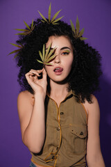 beautiful young woman with black curly hair and multi-colored makeup, with cannabis leaves in her...