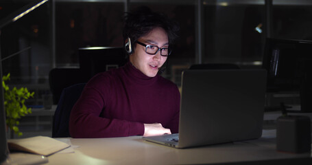 Asian businessman in headset working with computer late at night in client support service