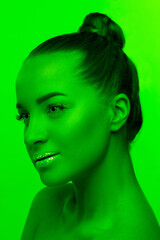 Fototapeta premium Modern. Handsome woman's portrait isolated on green studio background in neon light, monochrome. Beautiful female model. Concept of human emotions, facial expression, sales, ad, fashion and beauty.