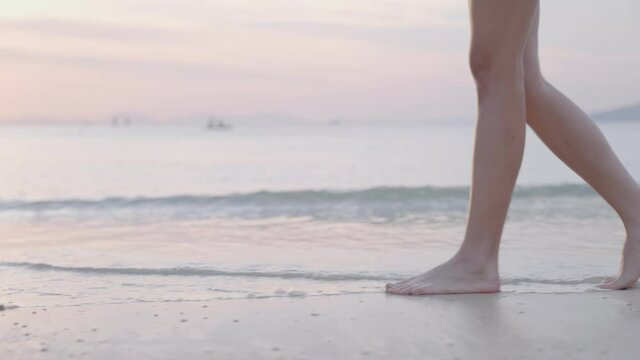 Young beautiful woman legs walking on beach while the sun is setting, relaxing calm in tropical summer holiday vacation, environment conservation, tropical island destination, side view low angle shot