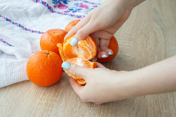 A girl with blue nails is peeling a tangerine. Women's hands and fruit tangerines