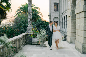 stylish wedding couple strolls against a backdrop of magnificent garden views. A young and stylish bride in a trendy wedding dress and a handsome groom at a wedding for two.