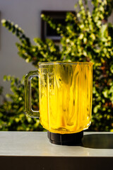 Glass blender with yellow liquid inside on the window sill against green tree background