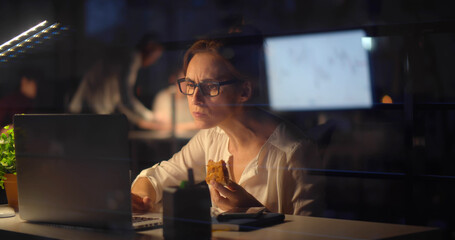 Businesswoman eating pie at desk working in office late in evening