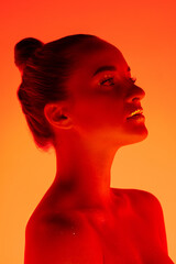 Calm. Handsome woman's portrait isolated on orange studio background in neon light, monochrome. Beautiful female model. Concept of human emotions, facial expression, sales, ad, fashion and beauty.