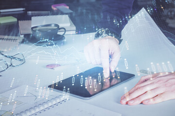 Double exposure of man's hands holding and using a digital device and forex graph drawing. Financial market concept.