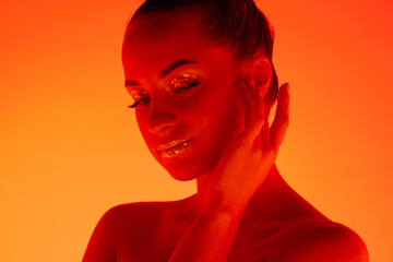 Icon. Handsome woman's portrait isolated on orange studio background in neon light, monochrome. Beautiful female model. Concept of human emotions, facial expression, sales, ad, fashion and beauty.