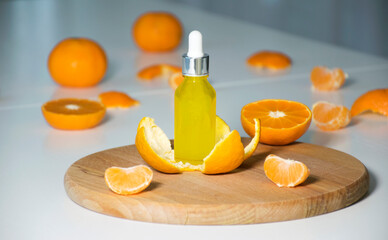 Vitamin C serum in cosmetic bottle in tangerine peel with mandarines on background. Citrus essential oil, face skin care, organic SPA cosmetics with herbal ingredients.