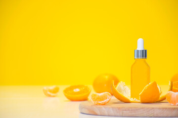 Vitamin C serum cosmetic bottle in tangerine peel with orange pieces on yellow background with copy space. Citrus essential oil, cosmetics aromatherapy. Organic SPA cosmetics with herbal ingredients.