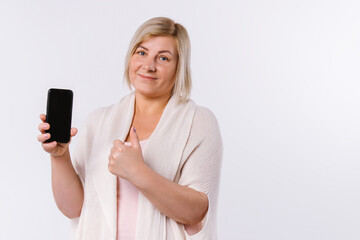 Fototapeta premium Senior woman holding smartphone in hands showing class at camera. White background and empty side space.
