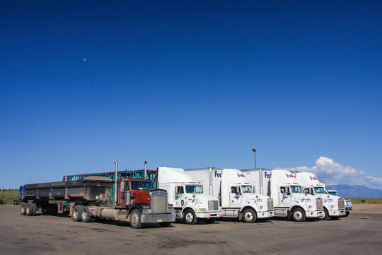 Fedex delivery trucks parked in row. Side view of cabins and trailers at highway rest stop under blue sky. American transport freight delivery vehicles