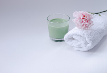 spa. white, terry towel with a pink flower on top and candles on a white background