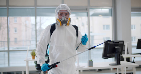 Contractor in safety uniform disinfecting office killing covid-19 virus