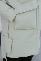 close up photo of white down coat with pocket detail and model hands close up photo