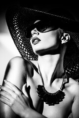 Fashion concept. Portrait of a beautiful woman in big hat and sunglasses in bright contrast light....