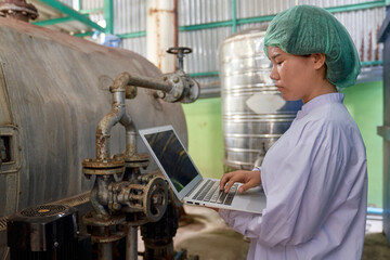 Asian Specialist is checking boiler machine with laptop in beverage industry
