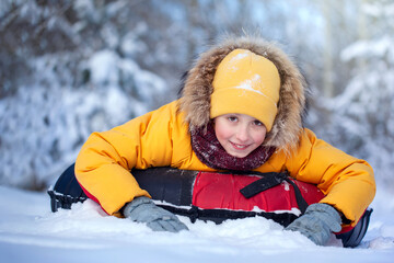 Fototapeta na wymiar Happy boy in winterwear smiling riding a tubing in winter park. Child sledding. Boy kid play outdoors in snow.