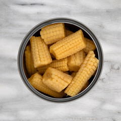 Top view of an open can filled with organic baby corn on a gray marble background.