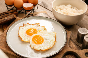 Plate with tasty eggs and rice in bowl on wooden background